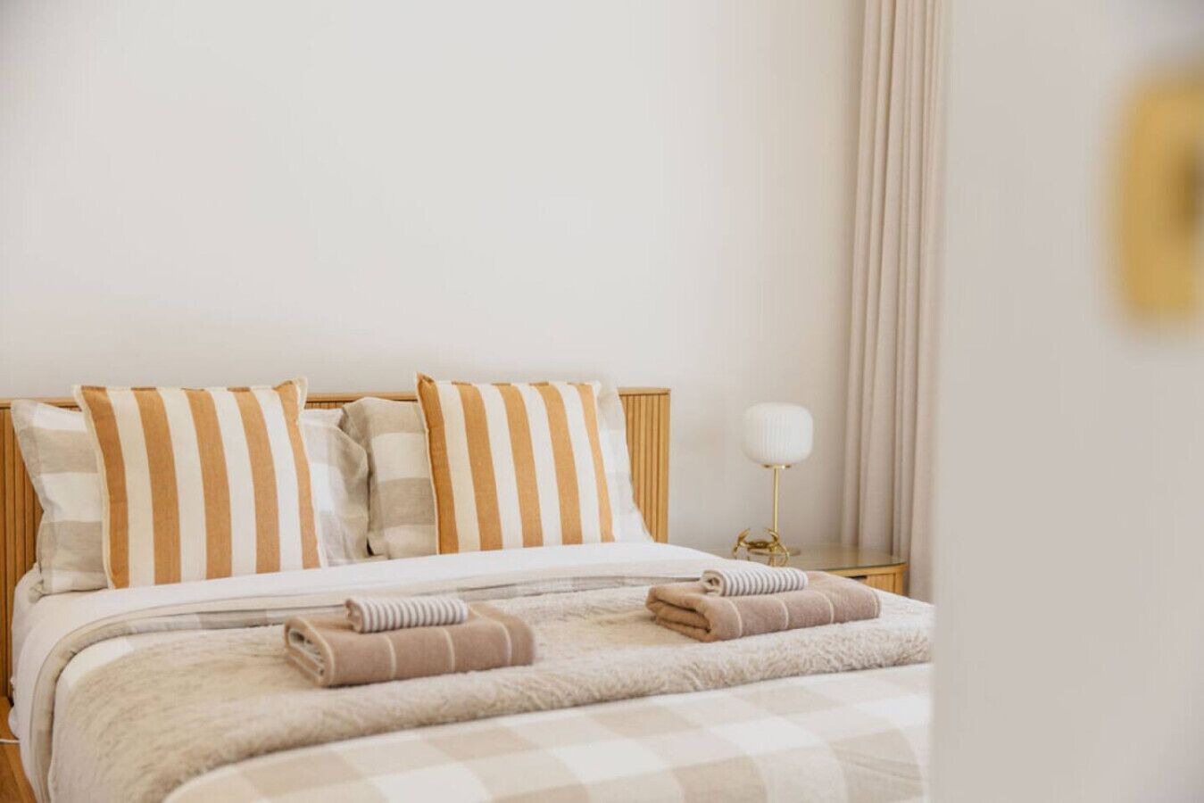 A hotel room with a bed, striped pillows, a bedside lamp, and a rolled towel on the bed.