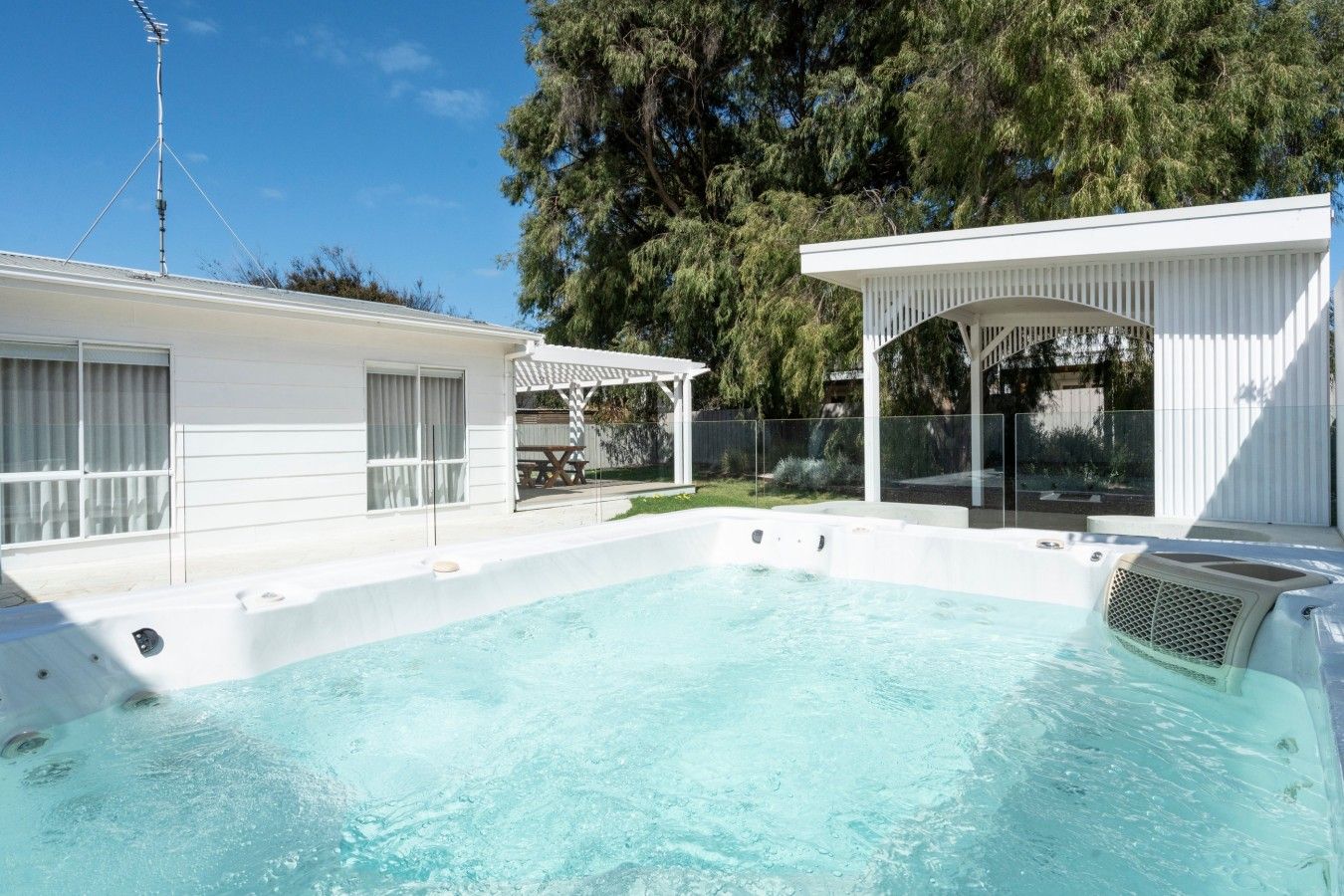 Una piscina con idromassaggio, un portico coperto e un edificio bianco con una pergola.