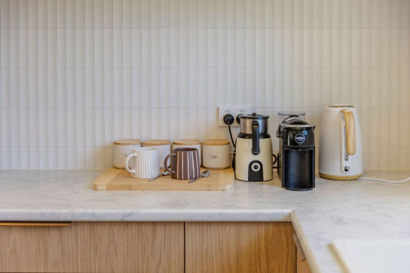 A kitchen counter with a coffee maker, a kettle, and several mugs.