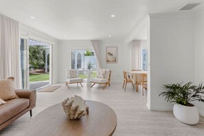 A spacious living room with a sofa, chairs, a dining table, and a large window. - Coastal Waters - Spa, Sleeps 8, Newly Renovated (499538) (Ocean Grove)