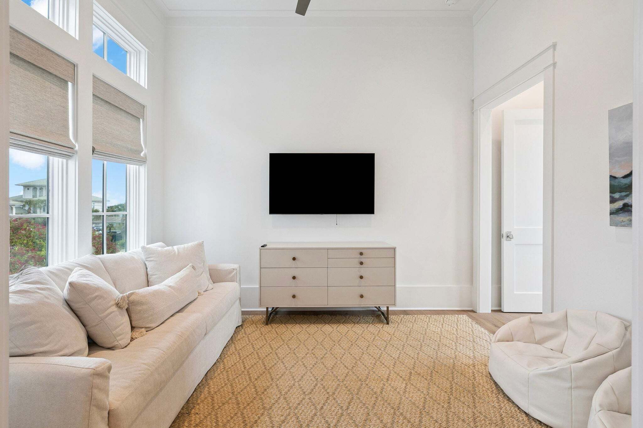 Un salon avec un canapé beige, un meuble blanc, un téléviseur à écran plat et un tapis à motifs.