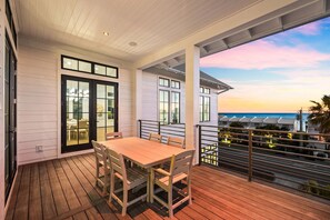 A wooden deck with a table and chairs, a covered area with a view of the ocean, and a building with large windows. - Sleeps 22! Private Pool, LSV/Golf Cart, & GULF VIEWS! Steps to Beach! (Santa Rosa Beach)