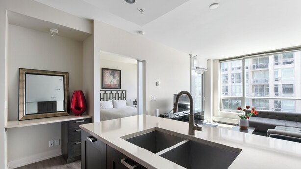 A modern kitchen with a double sink, a dining area with a sofa, and a large window offering a city view. - Modern Spacious Waterfront Condo Downtown Calgary (Calgary)