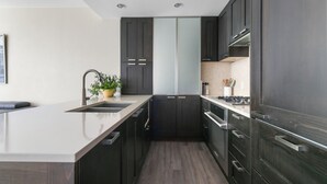 A modern kitchen with dark cabinetry, a central island, and a sink. - Modern Spacious Waterfront Condo Downtown Calgary (Calgary)