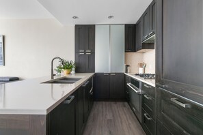 A modern kitchen with dark cabinetry, a central island, and a sink. - Modern Spacious Waterfront Condo Downtown Calgary (Calgary)