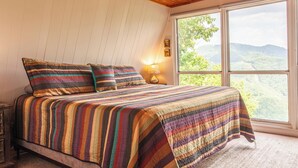 A bedroom with a large window, a wooden ceiling, and a bed with striped bedding. - Little Bear Cabin Robbinsville NC (Robbinsville)