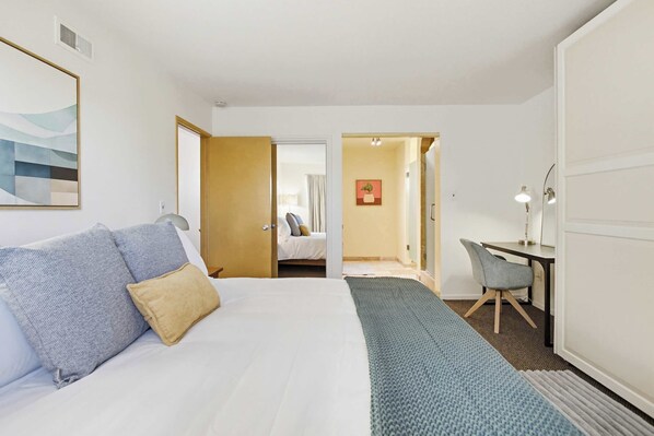 A hotel room with a bed, a desk, a chair, and a door leading to another room. - Sleeps 8 | 4BR | Fire Pit | Near UCSD & La Jolla (San Diego)
