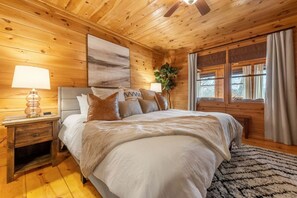 Une chambre à coucher aux murs lambrissés, avec un lit, des lampes de chevet, une plante et une fenêtre avec des rideaux.