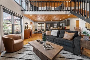 A spacious living area with a sofa, coffee table, and a staircase leading to an upper level. - Story Book Cabin| Mnt Views| Close to DT| Hot Tub (Blue Ridge)