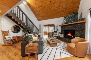 A modern living room with a fireplace, wooden staircase, and a cozy seating area. - Story Book Cabin| Mnt Views| Close to DT| Hot Tub (Blue Ridge)