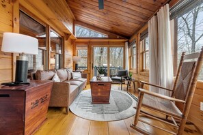 A wooden cabin interior with a sofa, a rocking chair, a coffee table, and a desk with a lamp. - Story Book Cabin| Mnt Views| Close to DT| Hot Tub (Blue Ridge)