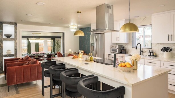 Uma cozinha moderna com ilha central, banquetas, eletrodomésticos de aço inoxidável e iluminação pendente.