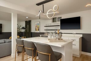 A modern kitchen with a central island, bar stools, a flat-screen TV, and a wine rack. - Entertainer's Dream with Hot Tub & Games (Arvada)