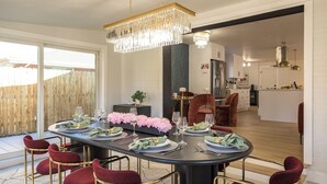 Uma área de refeições com uma grande mesa redonda, cadeiras estofadas em vermelho e um lustre.