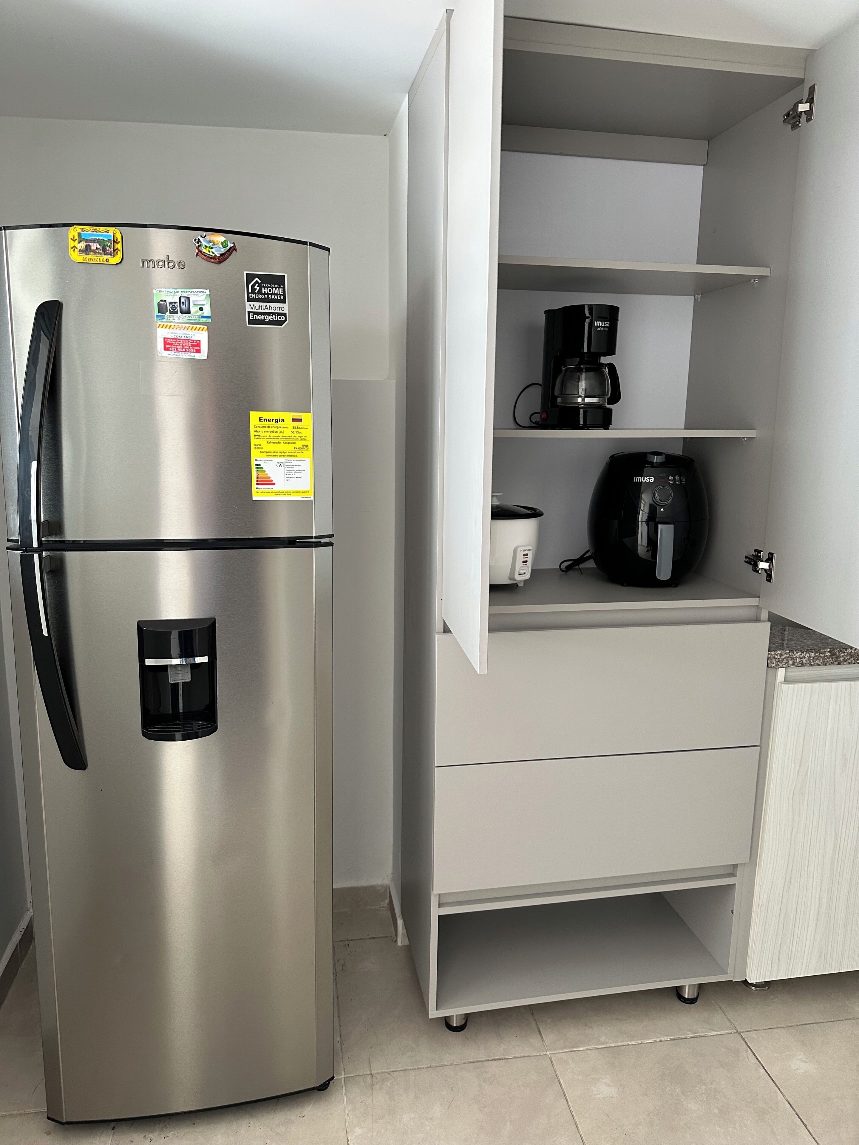 A stainless steel refrigerator with energy-saving stickers, a water dispenser, and a coffee maker on a white cabinet.