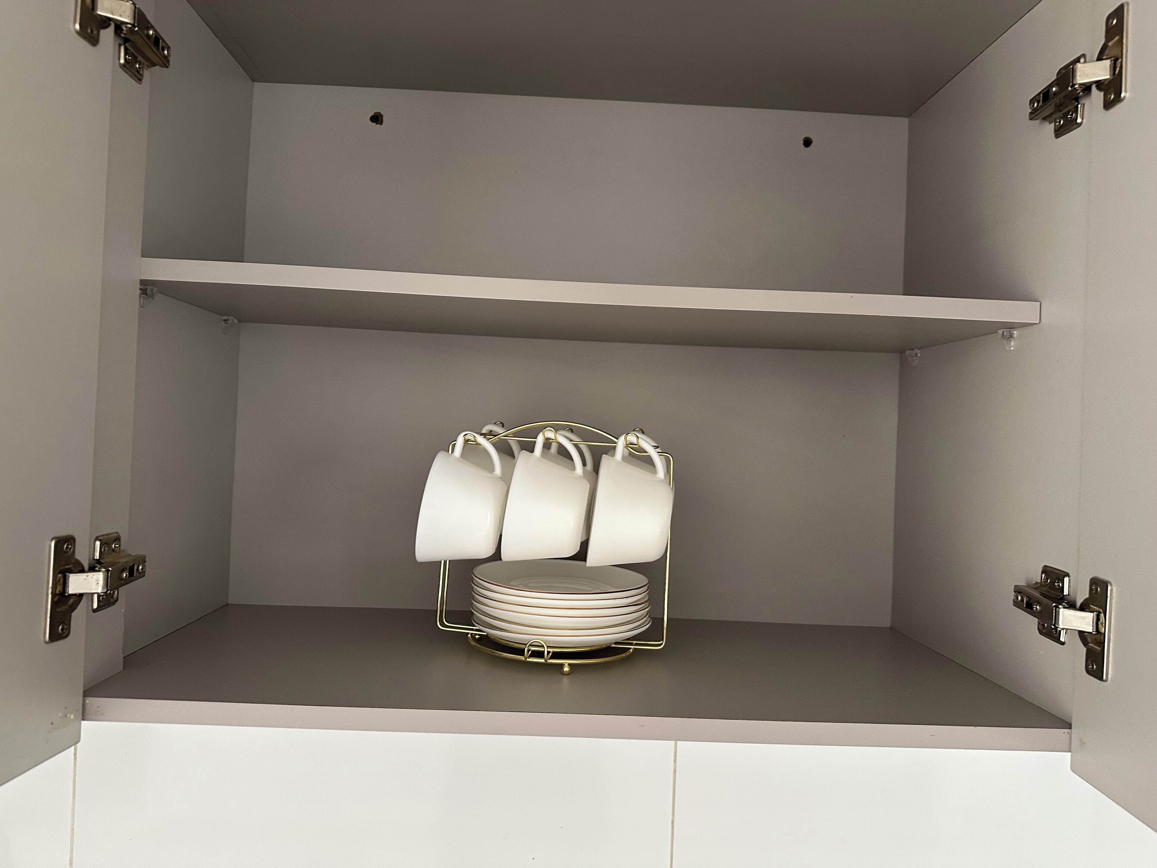 A kitchen with white cabinets, a metal rack holding white plates, and a grey countertop.