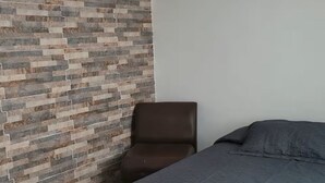 A bedroom with a bed, a chair, a tiled floor, and a wall with a textured pattern. - Enjoy a peaceful escape in the Coffee Region. (pereira)