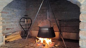 Un horno de ladrillo con una olla colgando de una cadena, leña y una rejilla metálica.