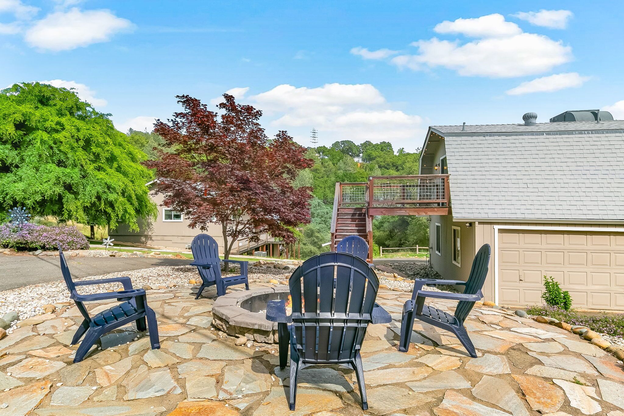 A stone patio with Adirondack chairs, a fire pit, and a garage.