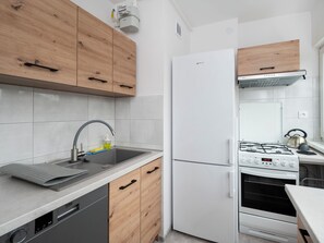 Una cocina moderna con lavavajillas integrado, pileta de acero inoxidable, muebles de madera, refrigerador blanco y estufa a gas.