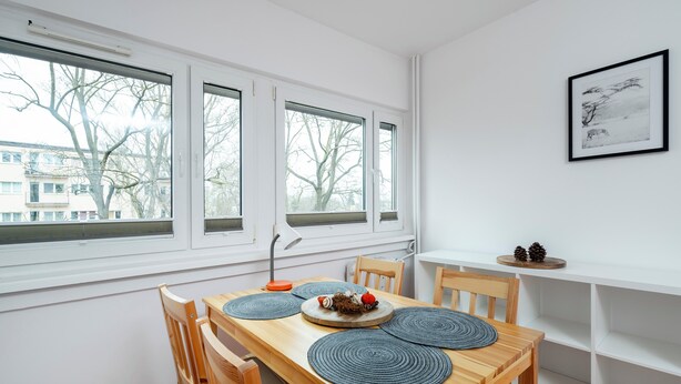 A dining area with a wooden table, chairs, and a view of trees through large windows. - Limanowskiego Harmony Apartment (Łódź)