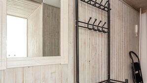 A room with a wooden wall, a metal rack with hooks, a mirror, and a black chair. - Limanowskiego Harmony Apartment (Łódź)
