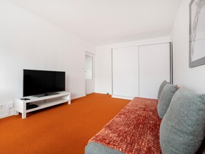 Una habitación con un televisor sobre un mueble blanco, una puerta corrediza y una alfombra estampada.