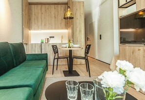 A modern living space with a green sofa, a dining table with chairs, a kitchen area, and a large window. - Sopot City Comfort Apartment #2 (Sopot)