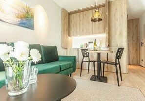 A modern living room with a green sofa, a round table, and a dining area with chairs. - Sopot City Comfort Apartment #2 (Sopot)