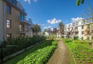 A residential building with a paved pathway, green garden beds, and a clear blue sky. - Sopot City Comfort Apartment #2 (Sopot)