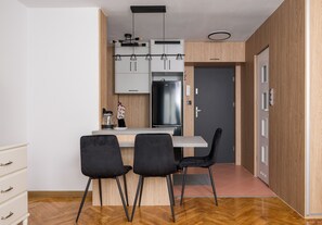 A modern kitchen with a central island, two black chairs, and wooden cabinetry. - Wola Anielewicza Deluxe Studio (Warszawa)