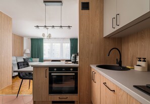 A compact kitchen with wooden cabinets, a built-in oven, a sink, and a dining area with a table and chairs. - Wola Anielewicza Deluxe Studio (Warszawa)