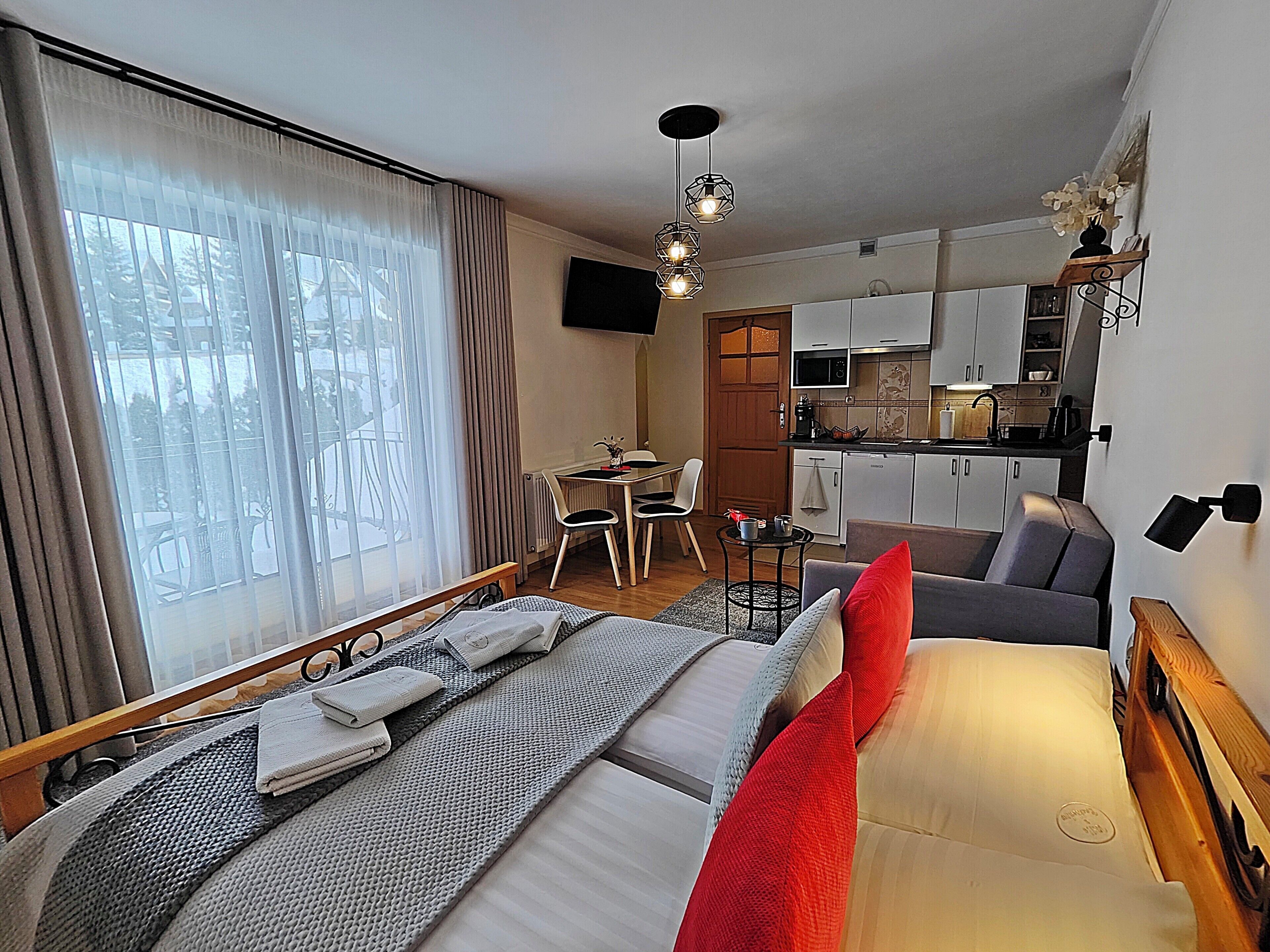 A hotel room with a bed, a small table, a sofa, a kitchen area, and a dining area.