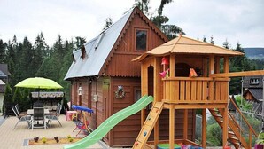 Une cabane en bois avec un toboggan, une table de pique-nique couverte et un petit espace aménagé en jardin.