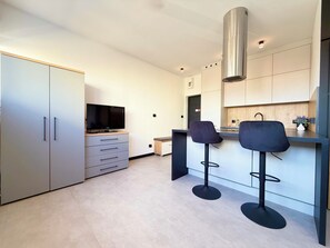 Eine moderne Küche mit Fernseher, zwei Barhocker und einer Edelstahl-Dunstabzugshaube.