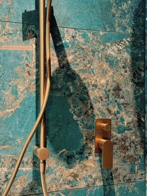 Ein Badezimmer mit blauer Marmorwand, einer goldfarbenen Duschbrause und einem goldenen Wasserhahn.