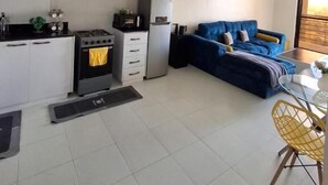 A compact kitchen with white cabinets, a stove, and a refrigerator. There is a blue sofa and a dining table with yellow chairs. - Heri Heights Ngong (Ngong)