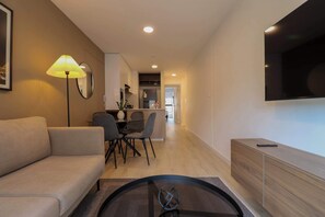 A modern living room with a sofa, a dining table with chairs, a coffee table, a TV mounted on the wall, and a kitchen area in the background. - w* | Modern & Cozy 2BR in the Heart of San Isidro (San Isidro)