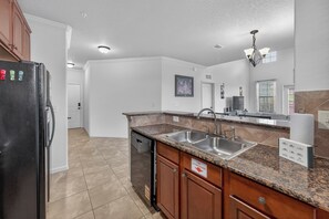 A kitchen with a black refrigerator, granite countertop, stainless steel sink, and wooden cabinets. - Charming Family-Friendly Condo Near Disney w Pool & Balcony (Davenport)