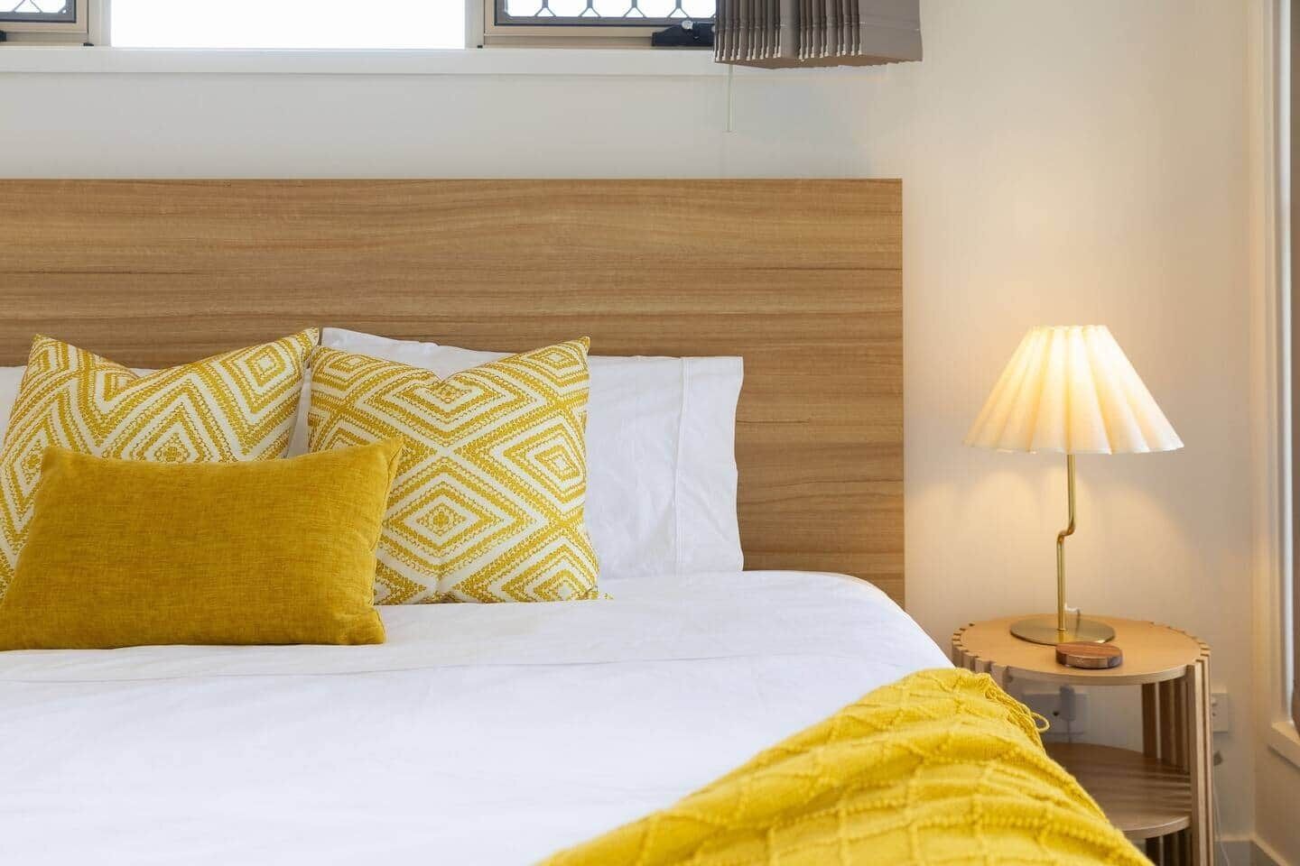 Een bed met gekleurde kussens, een bedlampje en een raam met uitzicht.