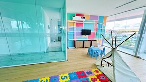 Une pièce moderne avec une cloison en verre, un espace de jeux coloré, une tente blanche et un téléviseur fixé au mur.