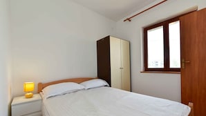 Ein Schlafzimmer mit Bett, Nachttisch, Lampe, Kleiderschrank und Fenster.
