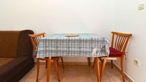 Ein Esstisch mit kariertem Tischläufer, zwei Holzstühle und eine braune Couch in einer Ecke eines Raumes mit gefliestem Boden.
