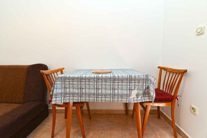 A dining table with a plaid tablecloth, two wooden chairs, and a brown sofa in a corner of a room with tiled flooring. - Holiday apartment with air conditioning (Fažana)