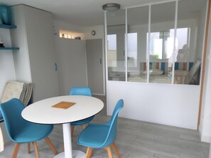 A modern room with a round white table, blue chairs, a large window, and a wardrobe. - Beautiful oceanfront apartment - sleeps 3 (FOURAS)
