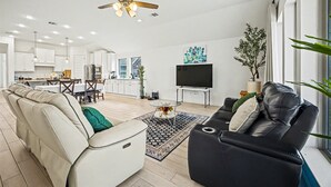 A modern living room with a sofa, a black leather couch, a ceiling fan, and a TV.