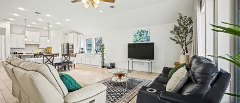 A modern living room with a sofa, a black leather couch, a ceiling fan, and a TV.