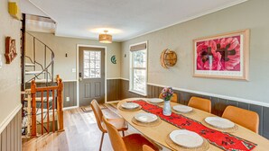Een eetgedeelte met een lange tafel gedekt voor vier personen, een trap en een deur naar buiten.