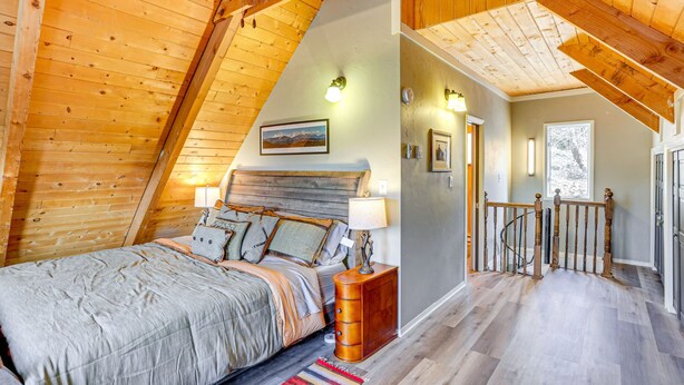 Een slaapkamer in loftstijl met een schuine plafond, een bed met veel kussens, een nachtkastje en een houten dressoir.
