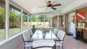 Un patio techado con una mesa y sillas, un ventilador de techo y vista al jardín trasero.